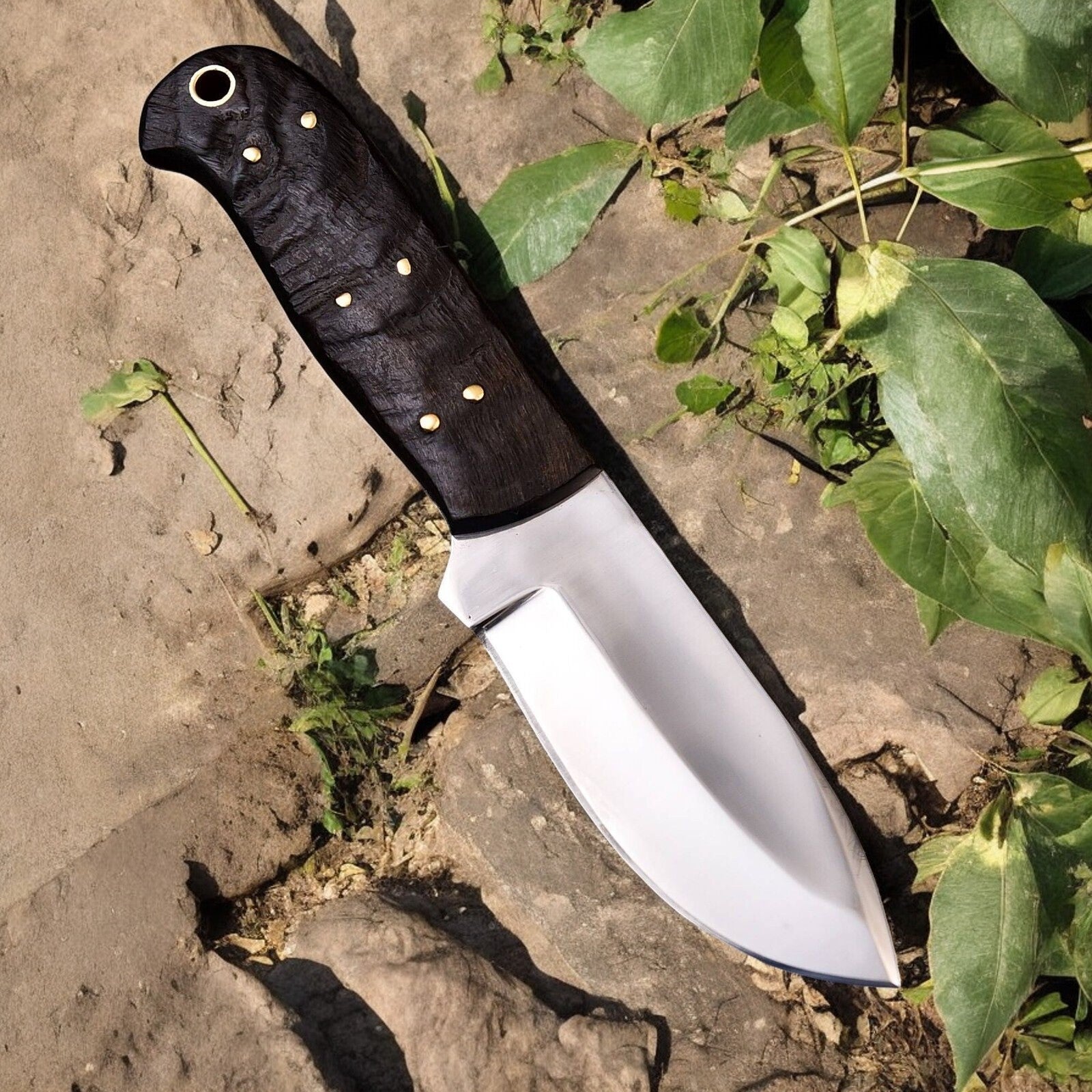 D2 steel hunt down knife displayed on a wooden surface in a natural setting.