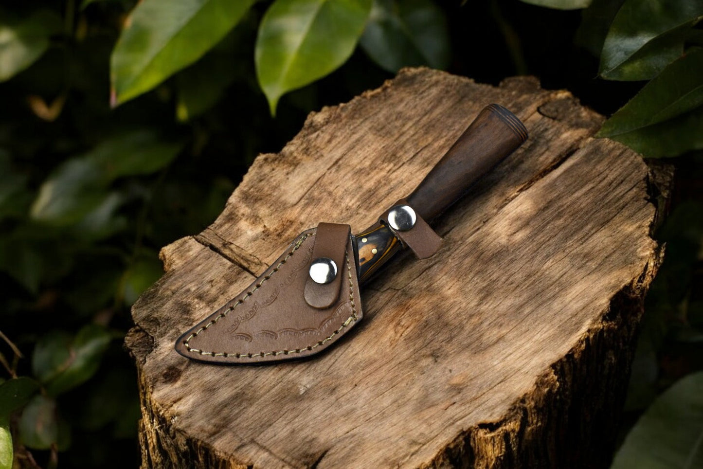 Damascus steel curved skinning knife displayed with its protective leather sheath.