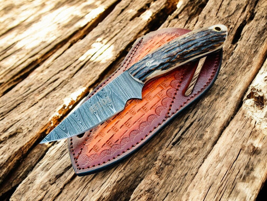 Knife with damascus blade and staghorn handle in a leather sheath on wooden background