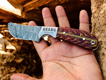 Hand holding a knife with 'Reeds Cattle Co.' branding against a natural background
