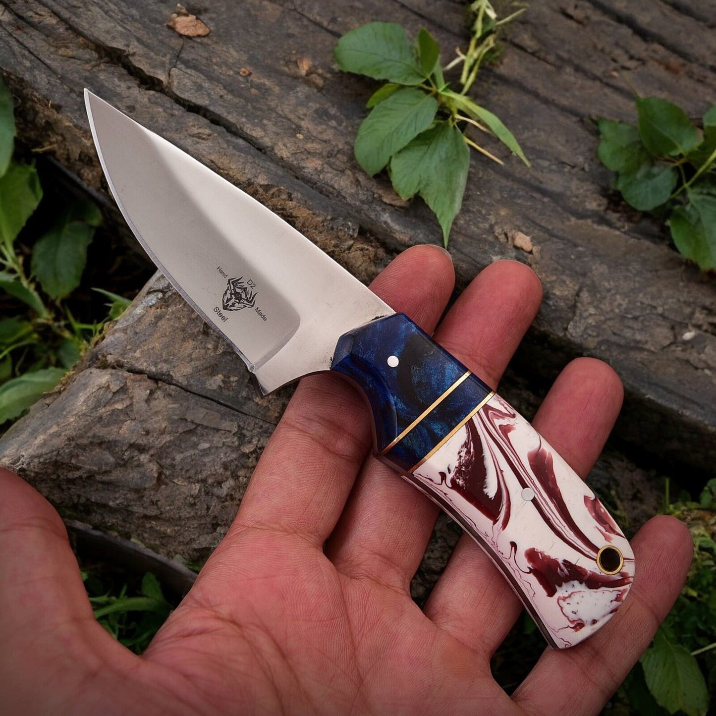 High carbon steel hunting knife with epoxy resin handle displayed on a natural surface.
