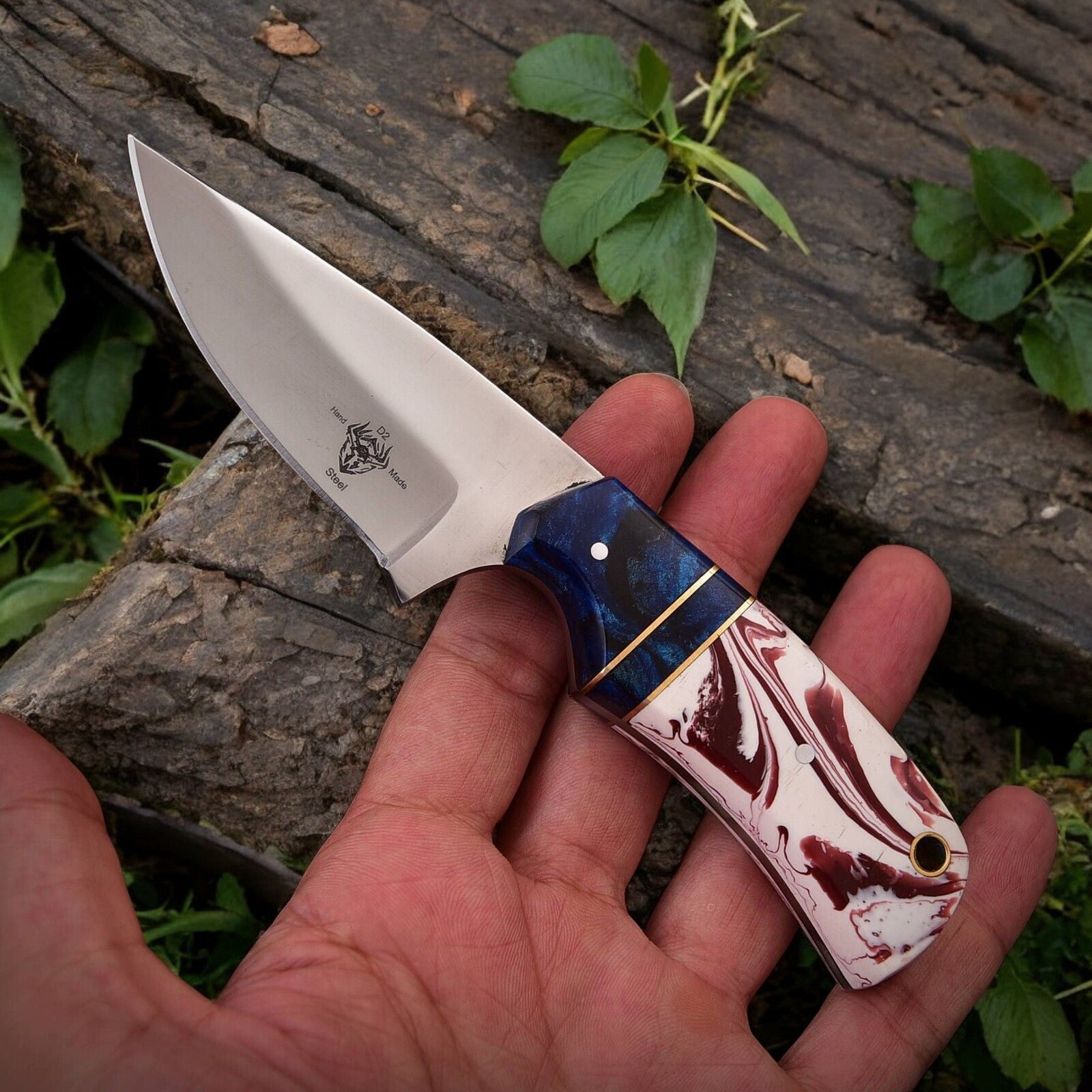 High carbon steel hunting knife with epoxy resin handle displayed on a natural surface.
