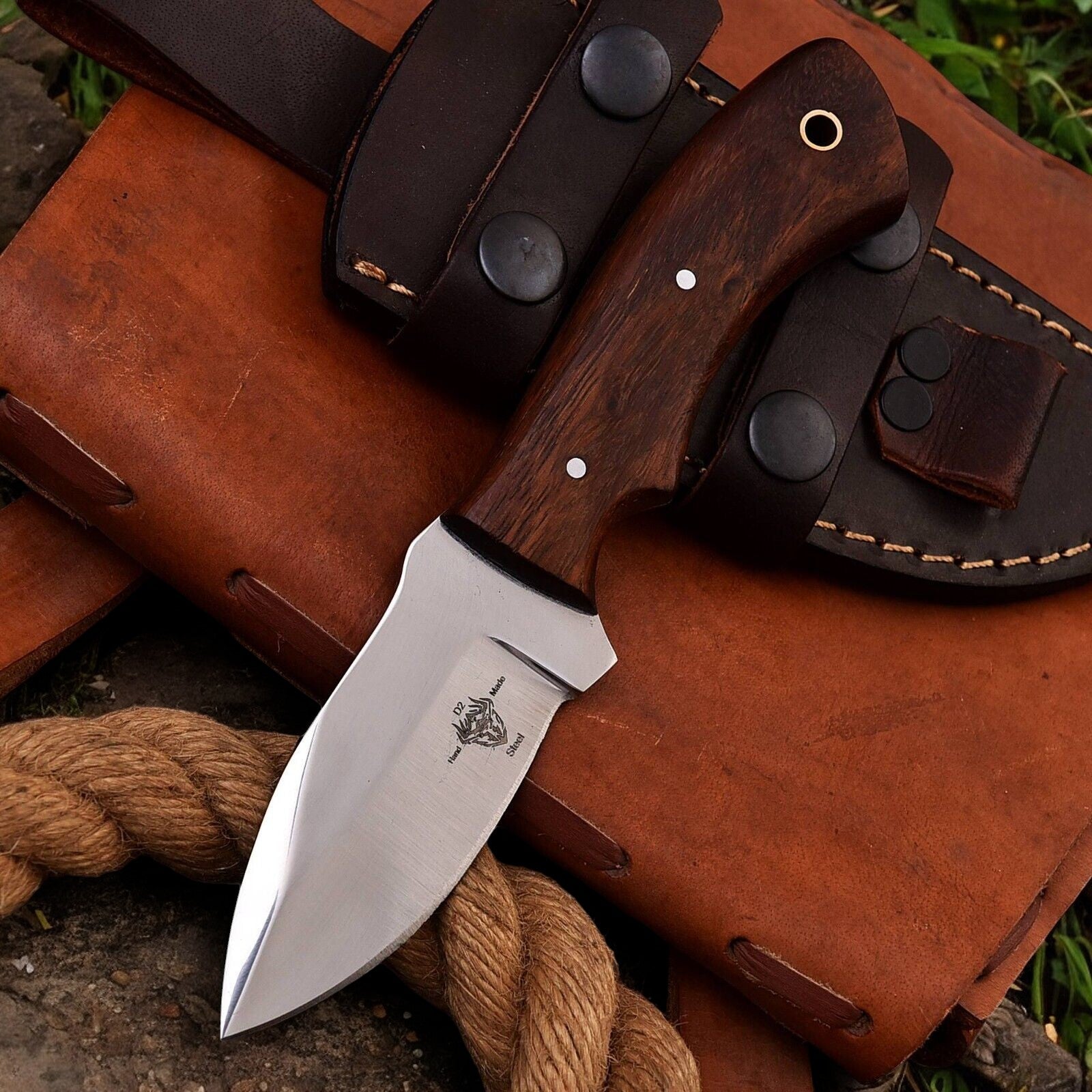 High carbon steel blade and rosewood handle on a handmade hunting knife displayed on a rustic surface.
