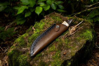 Damascus skinning knife resting inside its leather sheath.