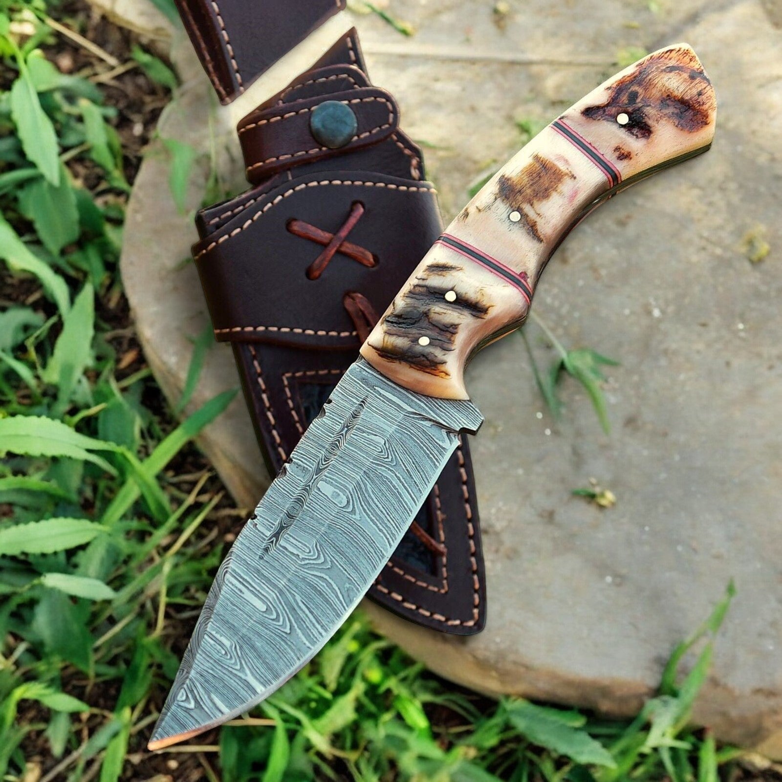 Custom Damascus hunting knife with blade and sheath displayed on wooden surface.





